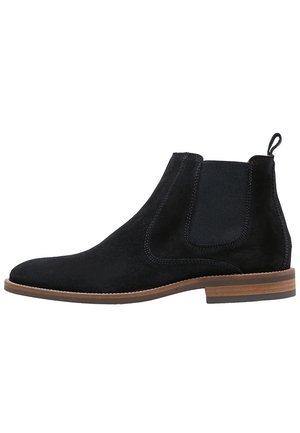 Bottine Chelsea en daim noir avec panneau latéral élastique, languette au talon, semelle en bois marron superposée et petit talon.