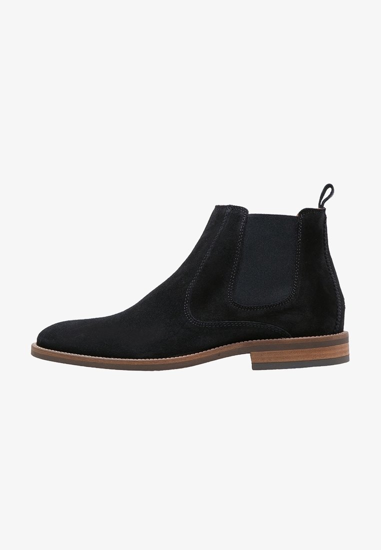 Bottine Chelsea en daim noir avec panneau latéral élastique, languette au talon, semelle en bois marron superposée et petit talon.