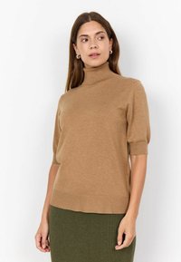 Kaki turtleneck pulover s kratkim rukavima, napravljen od mekog materijala. Rebrasti rub i glatka tekstura, uparen s tamnozelenom rebrastom suknjom.