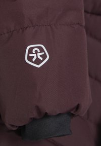Rúžová pufrová bunda s hladkou textúrou na rukáve, s bielym logom v šilde a čiernym rebrovaným manžetou.