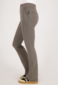 Uitlopende broeken in een geometrisch zwart-beige patroon. Bevat een middelhoge taille en twee achterzakken. Gemaakt van flexibele stof met een gladde textuur.