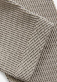 Tessuto rigato beige con una superficie texture. Primo piano che mostra una sezione piegata con cuciture e dettagli del motivo visibili.
