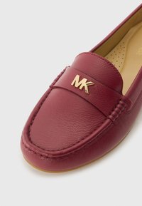 Burgundy leather moccasin with gold MK logo, stitched detailing along the sides, and a smooth interior surface for comfort.