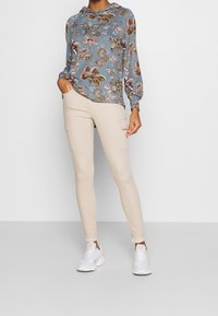 Modrá mikina s kapucí s květinovým vzorem, kombinovaná s béžovými pracovními kalhotami s bočními kapsami a bílými teniskami.