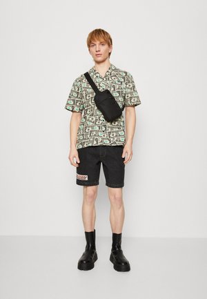 Camisa de manga corta con estampado de billetes de dólar en verde y negro, pantalones cortos de mezclilla negros con un logo rojo y botas de tobillo negras. Se incluye un bolso cruzado negro.