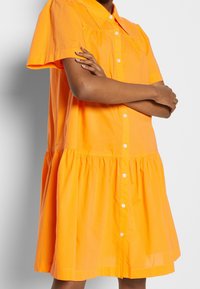 Robe à manches courtes et boutons en coton orange vif, avec une taille froncée et un ourlet évasé pour un ajustement décontracté.