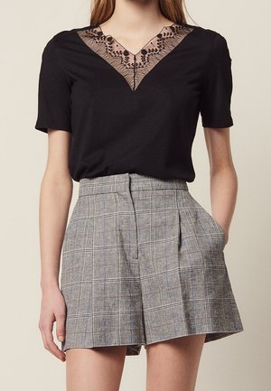 Sort top med korte ærmer og blonder ved V-halsen; kombineret med gråternet højtaljede shorts med læg og sidelommer.