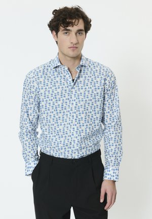 Hosszú ujjú ing fehér anyagból kék levélmintával, gombos gallérral és laza szabással, fekete nadrággal párosítva.