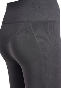 Högmidjade svarta leggings gjorda av slitstarkt, stretchigt tyg, med en ribbad textur och ett geometriskt mönster längs midjebandet.