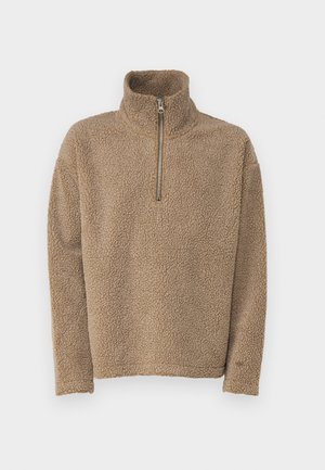 Pješački pulover od tan flisa s visokim ovratnikom i polu-zatvaračem. Ima meku, teksturiranu površinu i duge rukave, prikladno za ležerno nošenje.