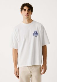 Witte katoenen t-shirt met een relaxte pasvorm, voorzien van een blauw grafisch ontwerp met de tekst "Red Bull Racing TEAM RECORDS" op de linkerkant van de borst.