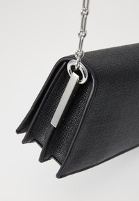 Svart teksturert clutch med en strukturert design og et sølvkjedehåndtak. Har en slank rektangulær form og hardwaredetaljer.