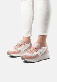 Sneakers sportive con tessuto bianco, accenti in suede rosa, dettagli grigi e suola in gomma texturizzata, dotate di lacci e marchio sulla linguetta.