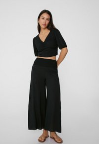 Top negro corto con mangas abullonadas cortas, con un frente fruncido. Combinado con pantalones anchos negros con una banda elástica en la cintura. Sandalias planas.