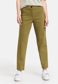 Olivově zelené kalhoty na míru se slim fit střihem, s kapsami na zip a zapínáním na knoflík, obuté s bílými platformovými teniskami. Hladká, strukturovaná tkanina.