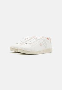 Sneakers sintetiche bianche con una texture liscia, caratterizzate da dettagli in rosa chiaro, fori laterali e lacci. Logo del brand sul lato.