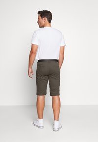 Calções khaki para homem, design slim-fit; tecido em mistura de algodão; textura lisa; combinados com uma t-shirt branca e ténis brancos.