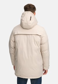 Giacca beige con cappuccio dal tessuto morbido, dotata di un ampio colletto, maniche lunghe e una schiena leggermente più lunga per una migliore copertura.