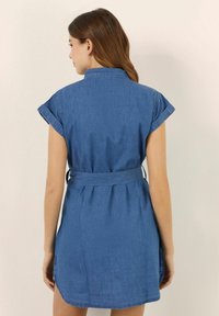 Denim-ruudullinen mekko, jossa on lyhyet, käännetyt hihat, vyöllinen vyötärö ja takana laskokset. Ominaisuuksiin kuuluu tasainen vaaleansininen väri ja suora helma.