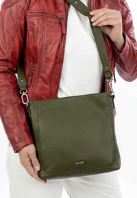 Green leather crossbody bag with a textured surface, rectangular shape, and a silver brand logo. Adjustable strap with metal hardware.