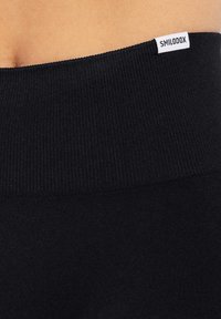 Czarne legginsy z wysokim stanem, z prążkowanym paskiem w talii i małą białą metką z logo "SMILODOX" w pobliżu górnej krawędzi.