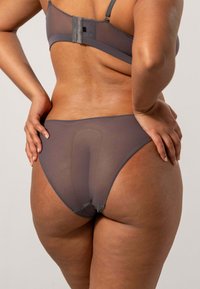 Set di lingerie grigio realizzato in tessuto a rete trasparente. La vista posteriore mostra una texture liscia con spalline regolabili e dettaglio di chiusura a gancio.