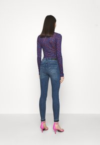 La blusa de manga larga presenta un patrón azul y rojo. Los pantalones vaqueros ajustados son de talle medio, tapered, con bolsillos traseros. Se combinan con sandalias de tacón alto rosas.