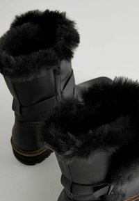 Bottes noires en fausse fourrure avec une finition texturée, dotées d'une fermeture éclair, d'une semelle robuste et d'un détail décoratif à la cheville.