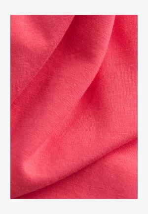 Korall rózsaszín anyag sima textúrával, fókuszált nézet a redők és hajtások részleteiről, ami puha, finom kötött anyagot mutat.