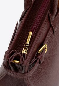 Bordowa skórzana torba na ramię o fakturowanej powierzchni, z zamknięciem na zamek błyskawiczny i złotymi akcentami. Posiada proste linie i wyraźny kształt.