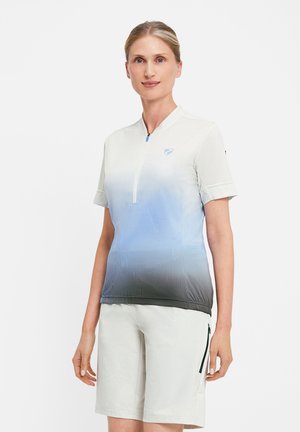 Frau steht und trägt ein kurzärmeliges, blau verlaufendes Zip-Up-Shirt sowie helle Shorts mit Reißverschlusstasche vor weißem Hintergrund.