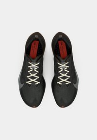 Schwarze Sportschuhe mit einem strukturierten Obermaterial aus Stoff, kontrastierenden weißen Schnürsenkeln und einem grauen Nike-Swoosh. Mit einer braunen Gummisohle.