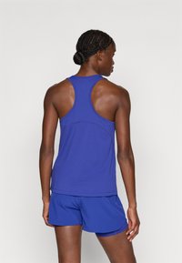 Kék sportos ujjatlan felső racerback kivitelezéssel, sima textúrával és kontrasztos varrással, kék rövidnadrággal, hasonló anyagból.