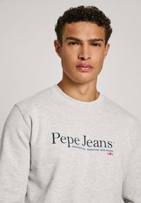 Sivi dukserica izrađena od mekanog materijala, s mornarsko plavim logom "Pepe Jeans" i natpisom "ORIGINAL DENIM BRAND" uz mali akcent britanske zastave.