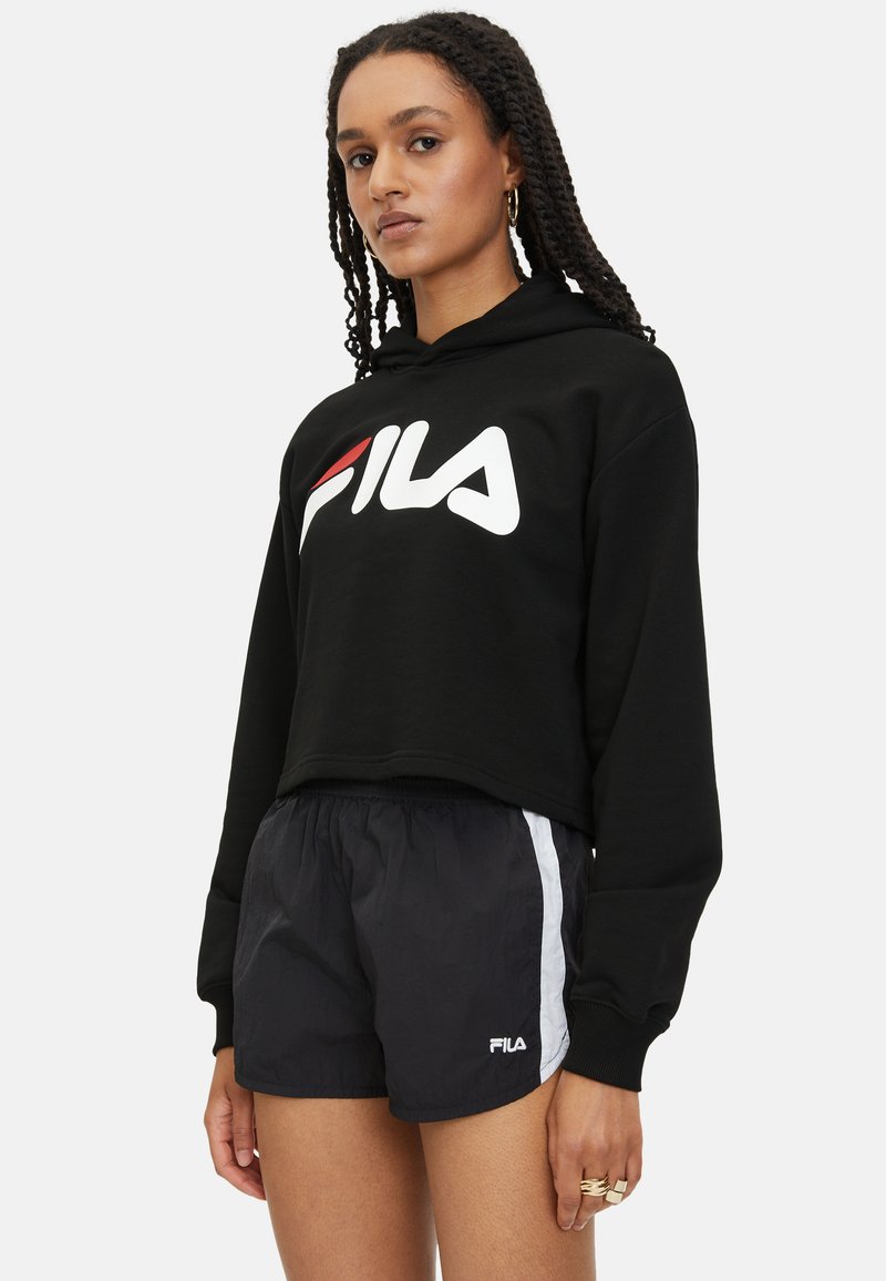 Sudadera recortada negra con logo blanco de FILA; combinada con pantalones cortos negros que tienen rayas laterales blancas y logo de FILA. Tela texturizada, corte relajado.