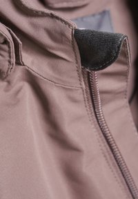 Brun tygjacka med en synlig dragkedjedetalj, som har ett mjukt innerfoder och sömmar, vilket visar en slät och hållbar textur.