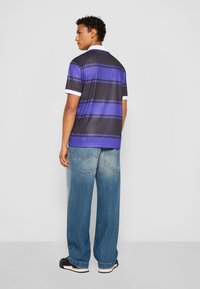 Kortærmet polo-shirt i sort med vandrette lilla striber og hvid krave, parret med lysblå vidde jeans og sorte sneakers.