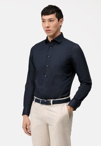 Navyblauwe shirt met lange mouwen en een aansluitend design, met knopen aan de voorkant, gecombineerd met beige broeken en een geweven, donkerblauwe riem.