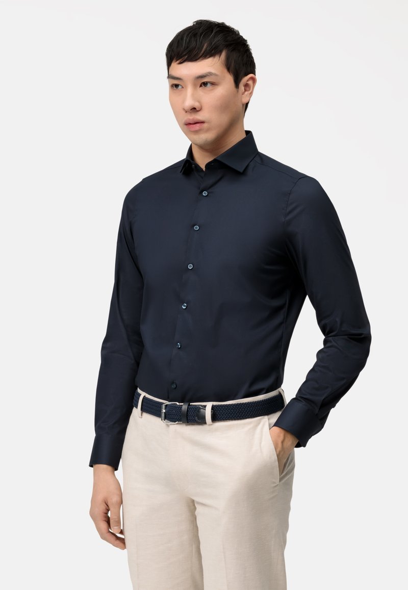 Navyblauwe shirt met lange mouwen en een aansluitend design, met knopen aan de voorkant, gecombineerd met beige broeken en een geweven, donkerblauwe riem.