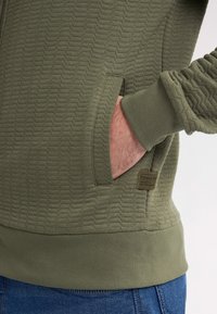 Groene hoodie met een patroon en een textuur, kangoeroezak, geribbelde manchetten en logo-label. Gemaakt van zacht materiaal met een relaxte pasvorm.