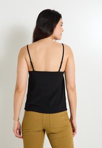 Top negro sin mangas con tirantes finos, con una textura suave y un corte relajado, combinado con pantalones color marrón claro de cintura alta y costuras traseras visibles.