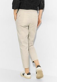 Beige byxor med elastiskt midjeband har en avsmalnande design, bakfickor, och är parat med vita sneakers med svarta detaljer.