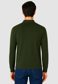 Polo verde a maniche lunghe con tessuto testurizzato, colletto e polsini a costine, e orlo dritto, abbinato a jeans in denim blu.