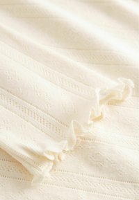 Cream fabric featuring textured stripes and delicate eyelet patterns, with a ruffled edge adding a soft detail.