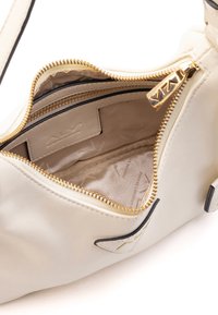 Kremowa torebka na ramię z syntetycznej skóry, wnętrze z złotym zamkiem, beżowa podszewka i czarne akcenty. Posiada wiele przegrod.