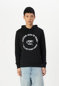 Schwarzer Hoodie aus Baumwollmischung mit grafischem Text. Verfügt über eine Kängurutasche und eine Kapuze mit Kordelzug. Kombiniert mit hellblauen Jeans.