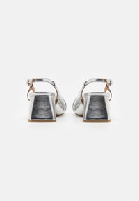 Sandali con tacco alto metallici argento, con cinturino alla caviglia e tacco a blocco. Texture liscia, con una base solida e una chiusura a fibbia regolabile.