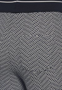 Tissu à motif zigzag bleu marine et blanc avec une ceinture élastique noire, vue rapprochée du matériau textile texturé.