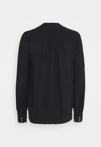 Schwarze Bluse mit langen Ärmeln, feinem strukturiertem Punktmuster, Rückenpasse mit Falten und knöpfbaren Manschetten, auf einem weißen Hintergrund präsentiert.