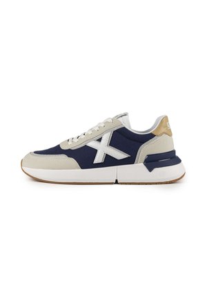 Zapatillas de lona navy con detalles en gamuza gris, suela de goma blanca y un logo blanco prominente. Cuenta con un collar acolchado y diseño de cordones.